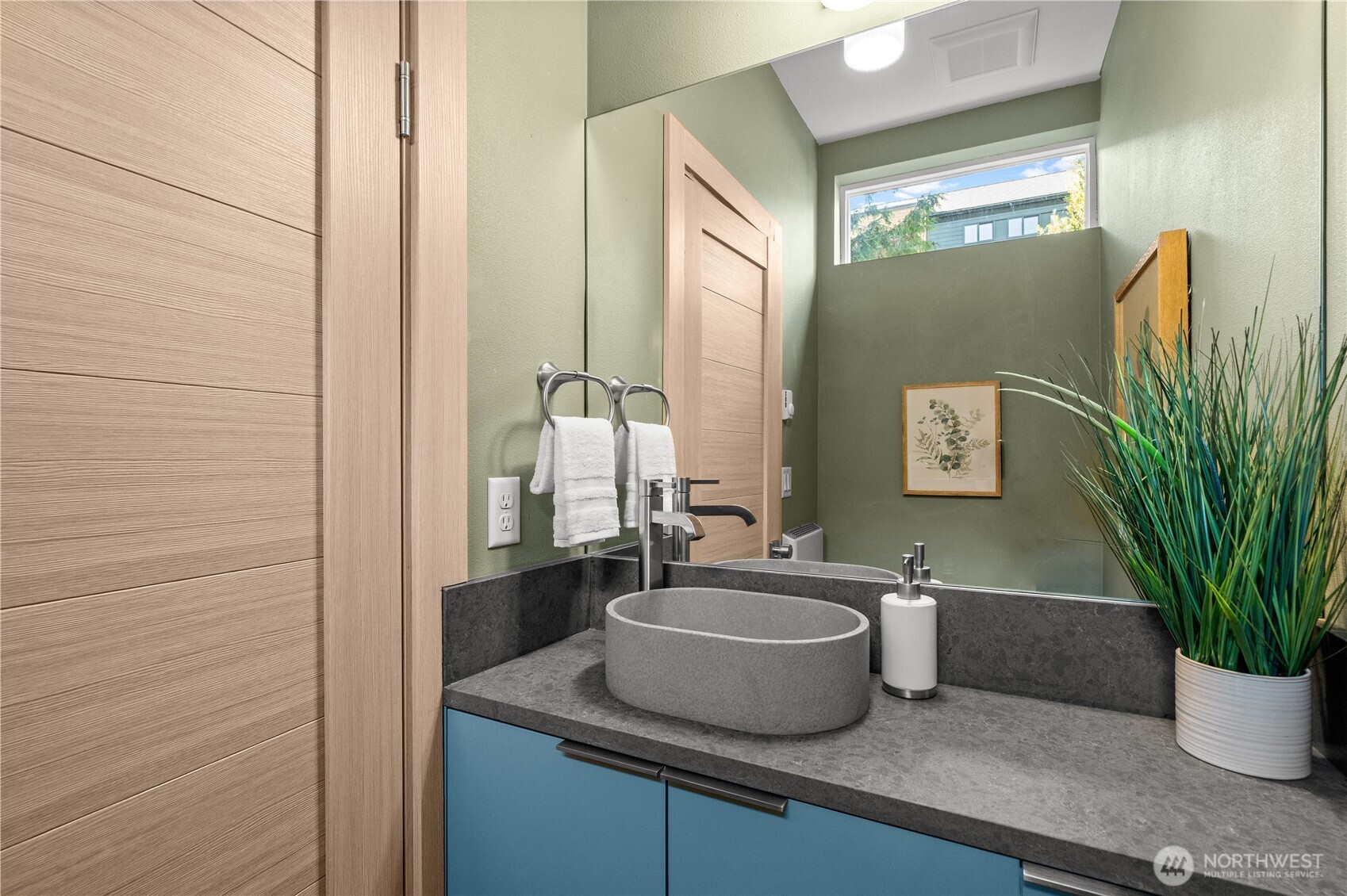 Bathroom vanity with a round vessel sink, blue cabinet, gray stone counter, and large mirror.
