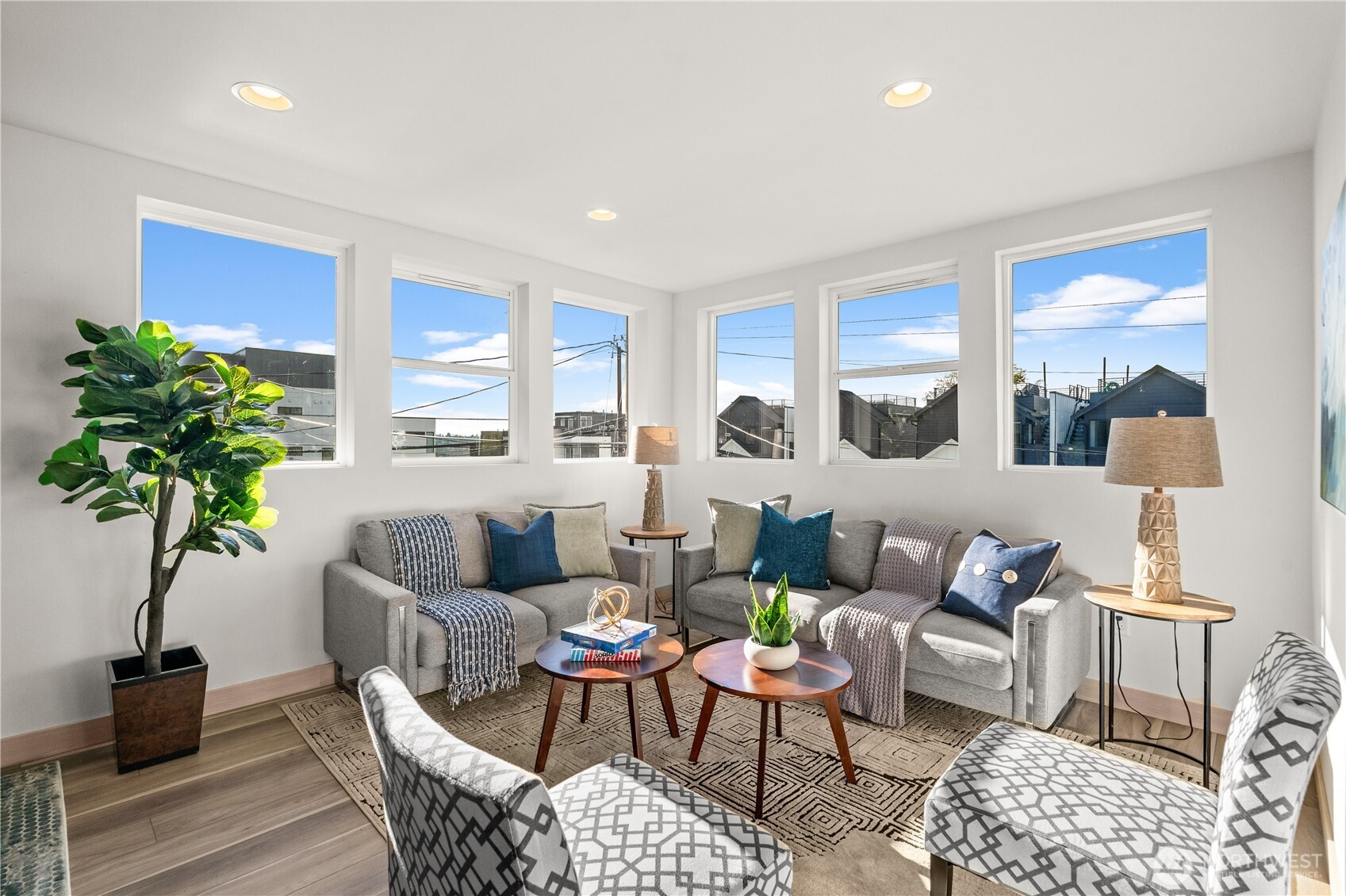 Staged living room with gray sofas, patterned armchairs, and six large windows.