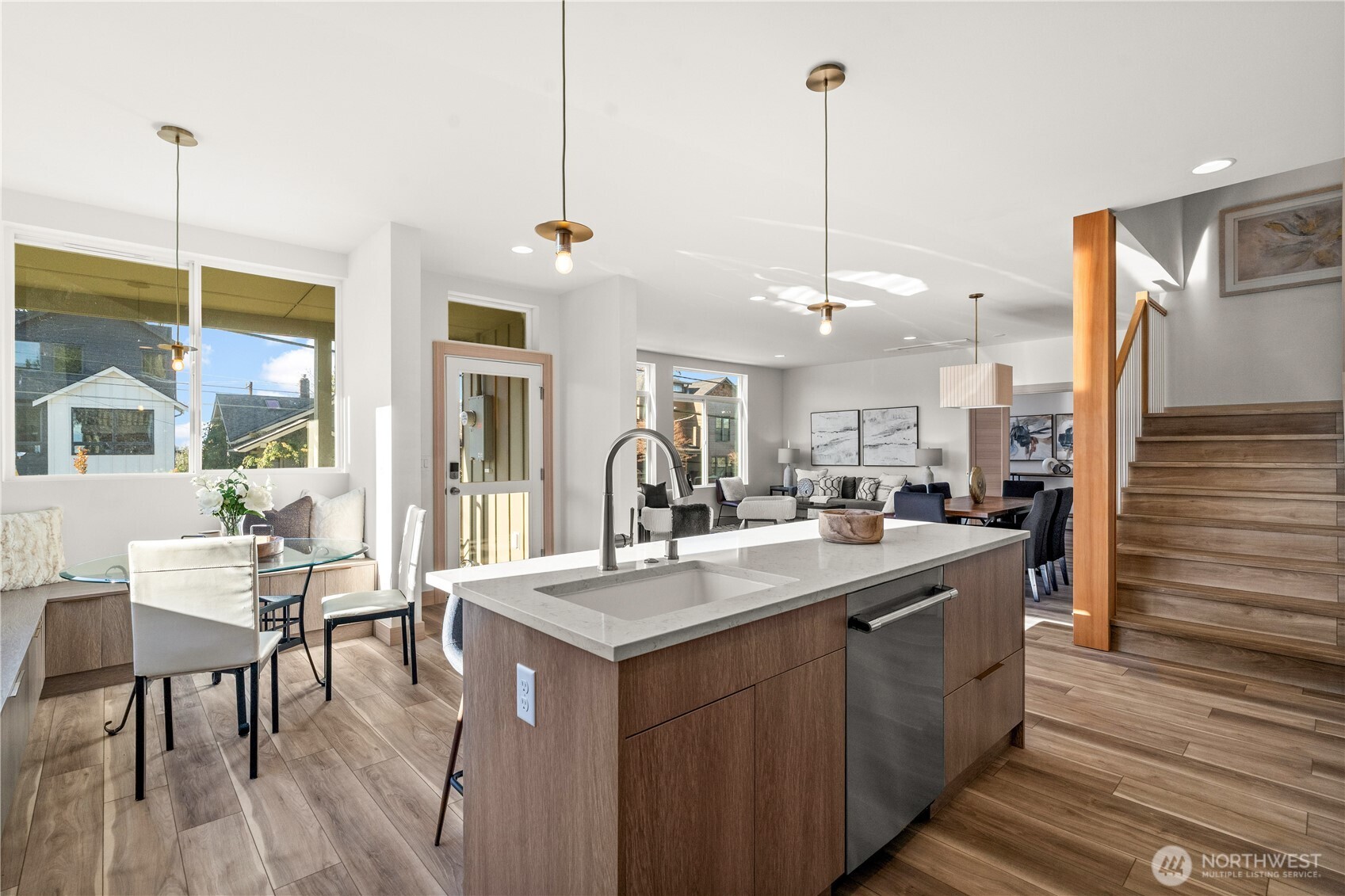 Open-plan kitchen with a large wood island, dining nook by the windows, and staircase beside the living area.