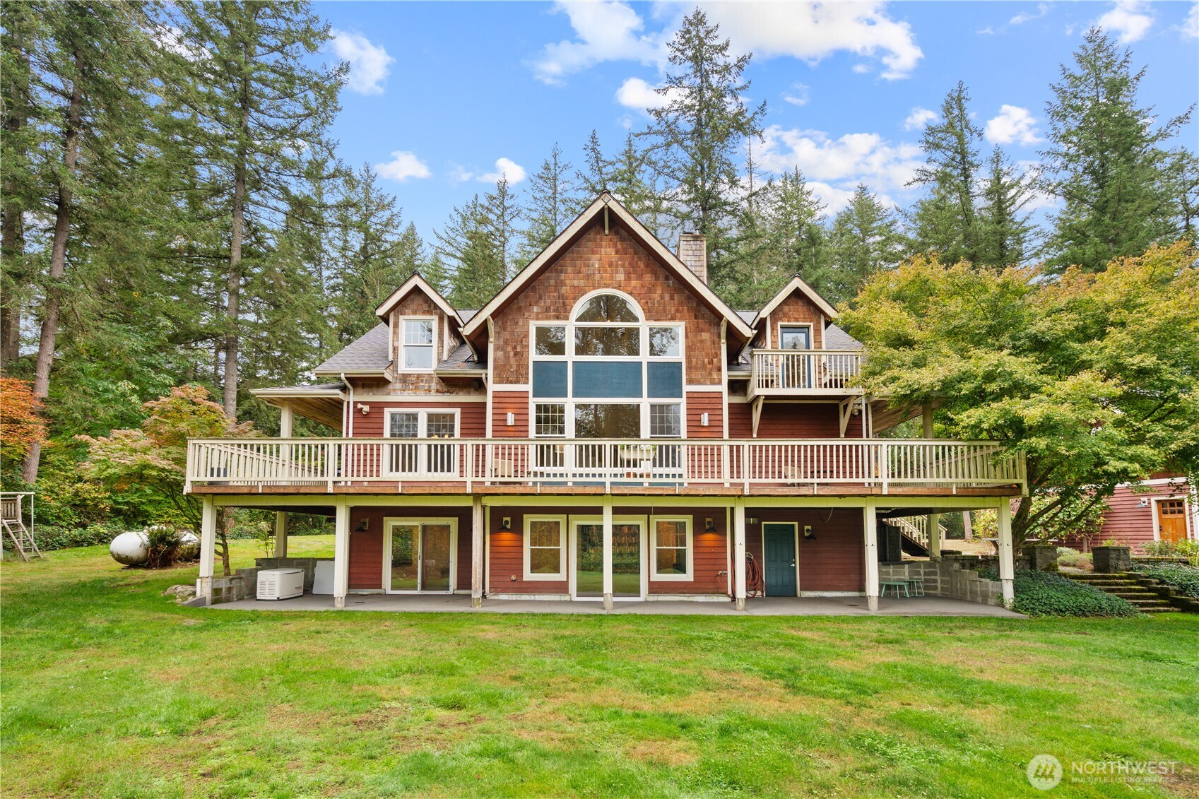 Cedar-shingle house with a broad raised deck, surrounded by mature trees and lawn.