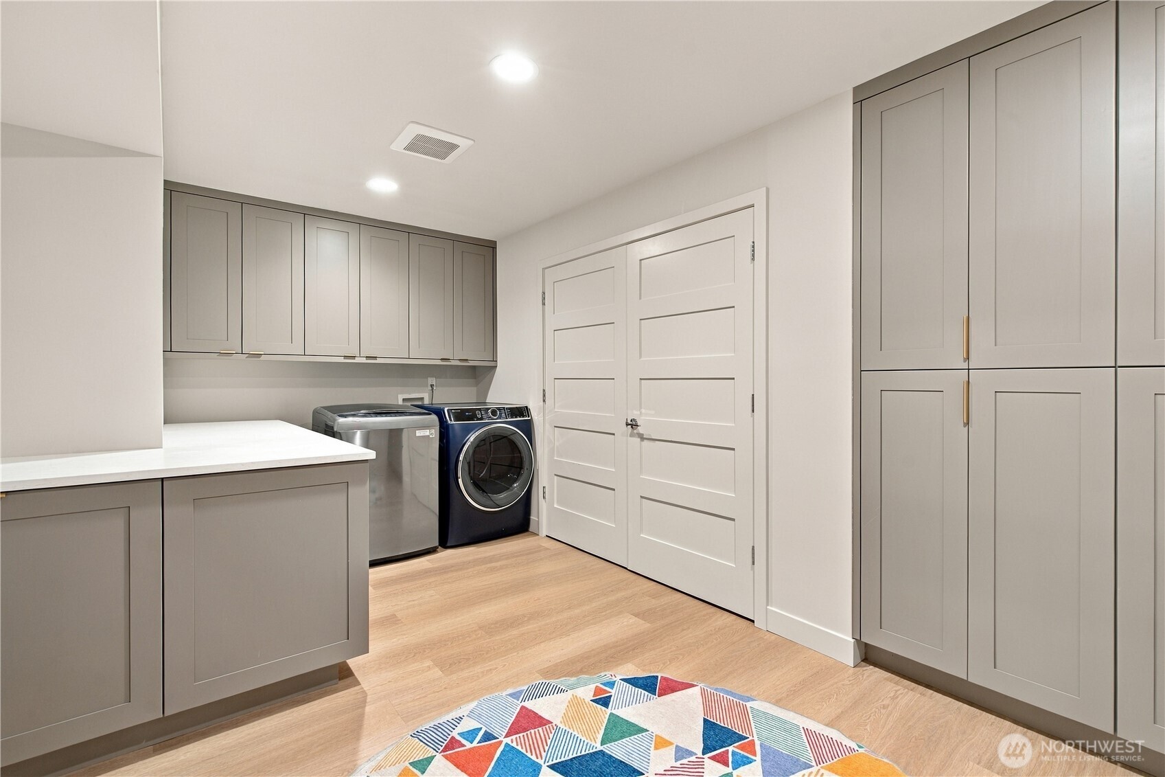 Laundry room with gray built-in cabinets, washer and dryer, and a colorful geometric rug.