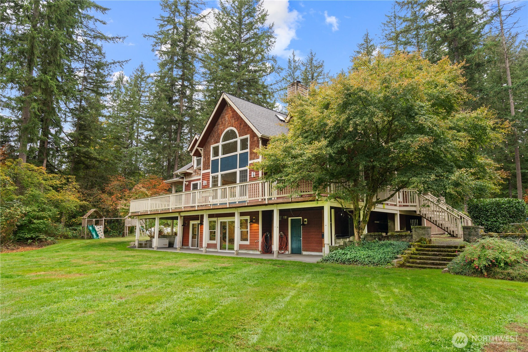 Wood-sided home with a large elevated deck overlooking a broad lawn and wooded backyard.