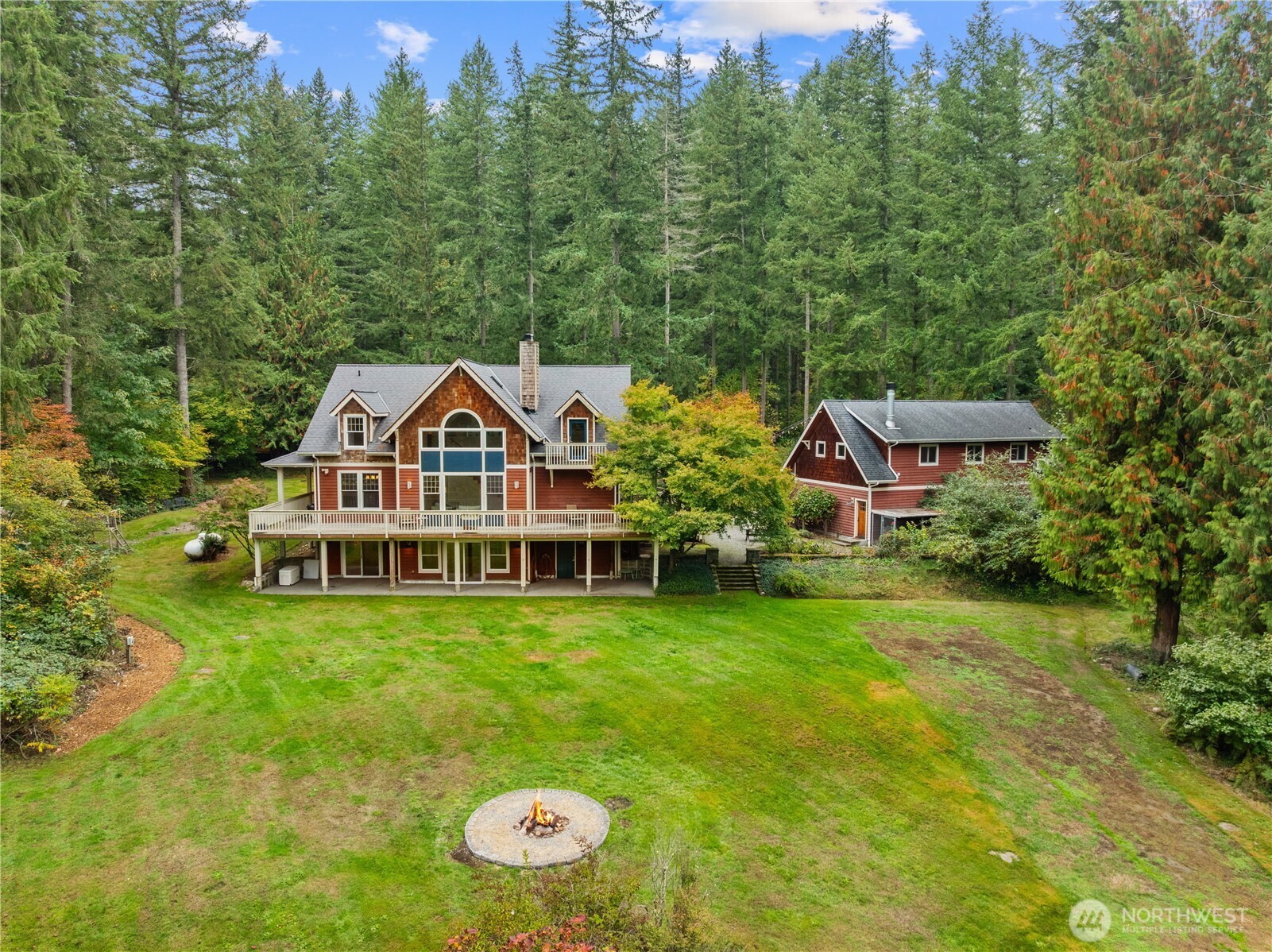 Aerial view of two red buildings amid tall trees, with a broad lawn and circular fire pit.