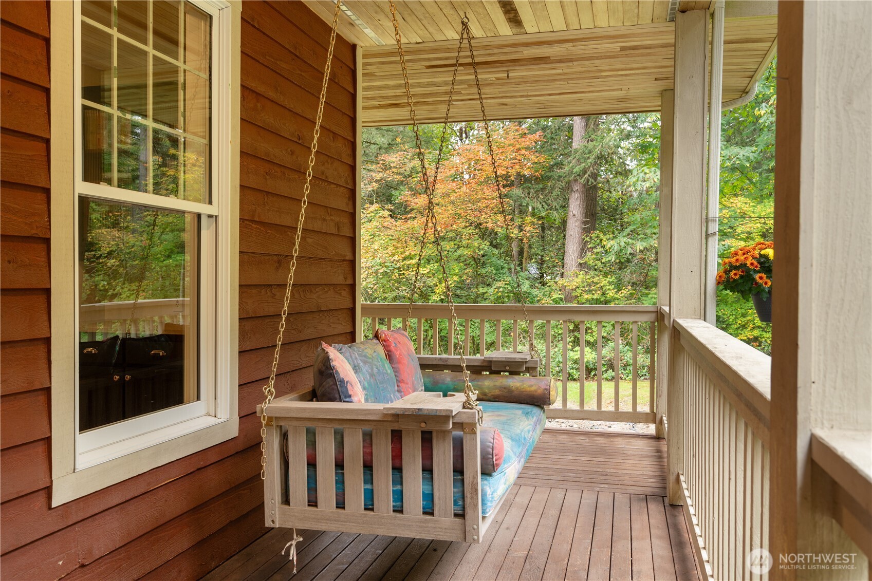 Covered porch with a cushioned hanging swing overlooking autumn trees.