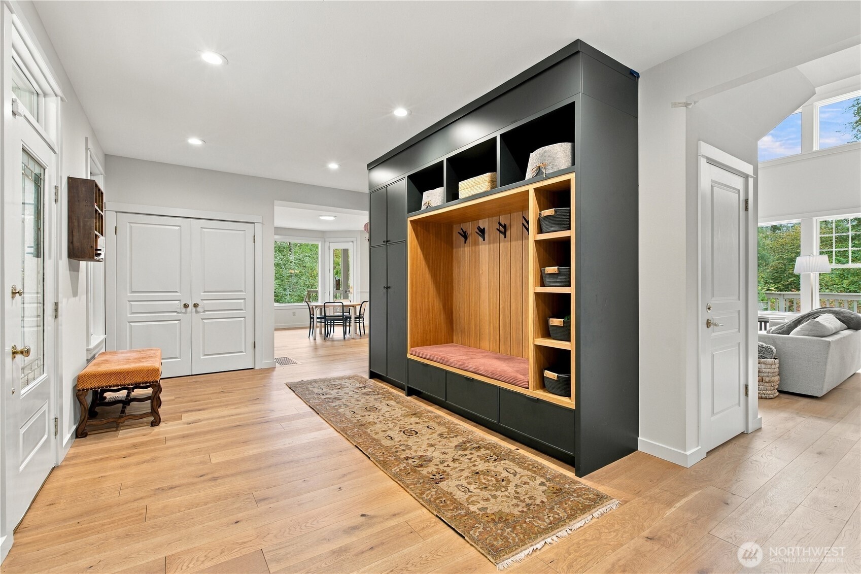 Entry hall with charcoal built-in mudroom cabinetry, wood bench, hooks, and light oak floors.