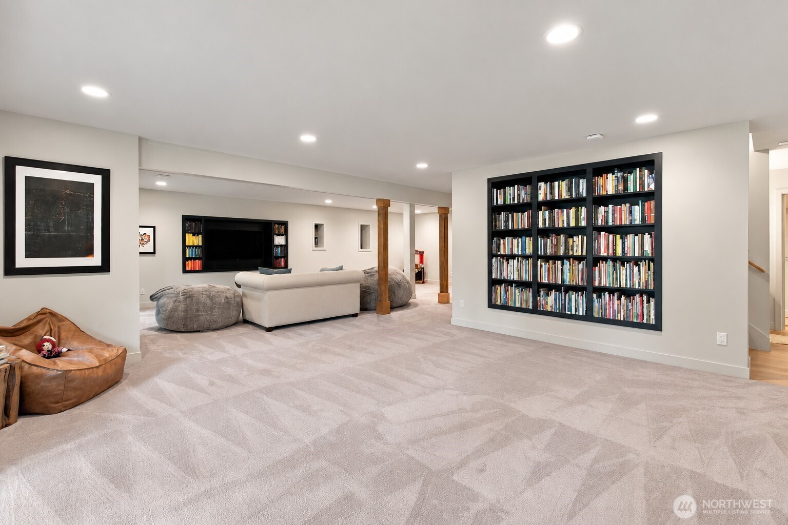 Basement family room with a wall of bookshelves, recessed TV area, and spacious patterned carpet.