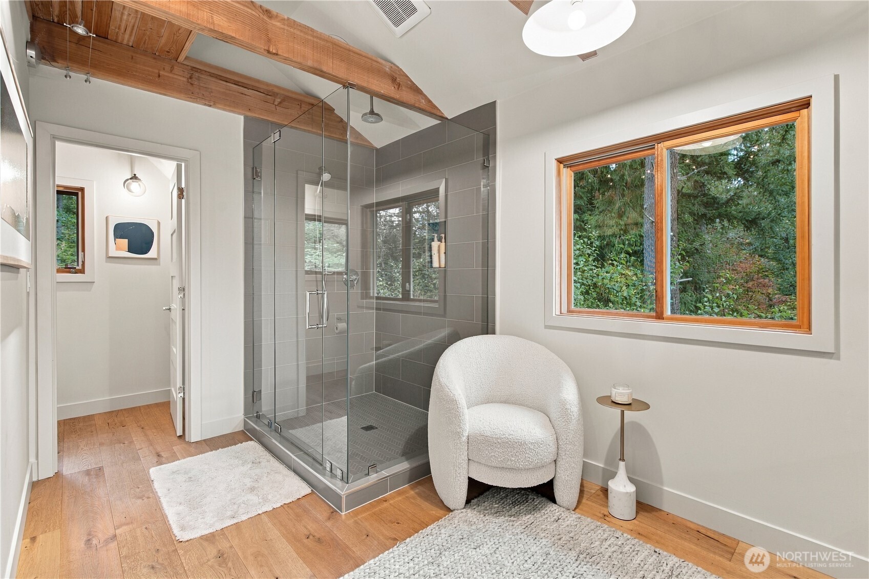 Bathroom with a glass shower, exposed wood beams, and a window overlooking trees.