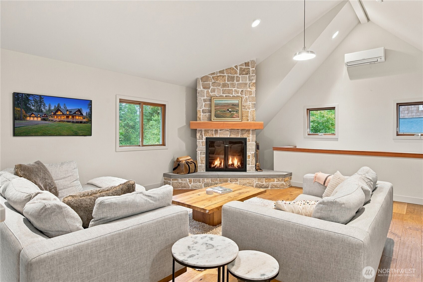 Furnished living room with a vaulted ceiling and a lit stone-surround fireplace.