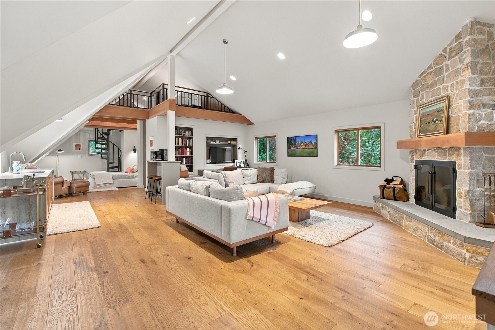 Vaulted living room with a stone fireplace, loft railing, oak floors, and white sectional sofa.