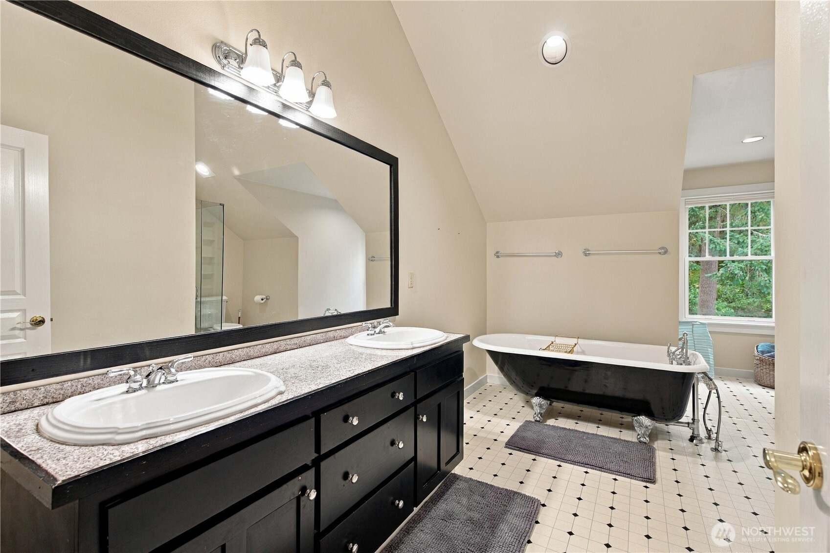 Bathroom with a black double vanity and a freestanding clawfoot tub beside a window.