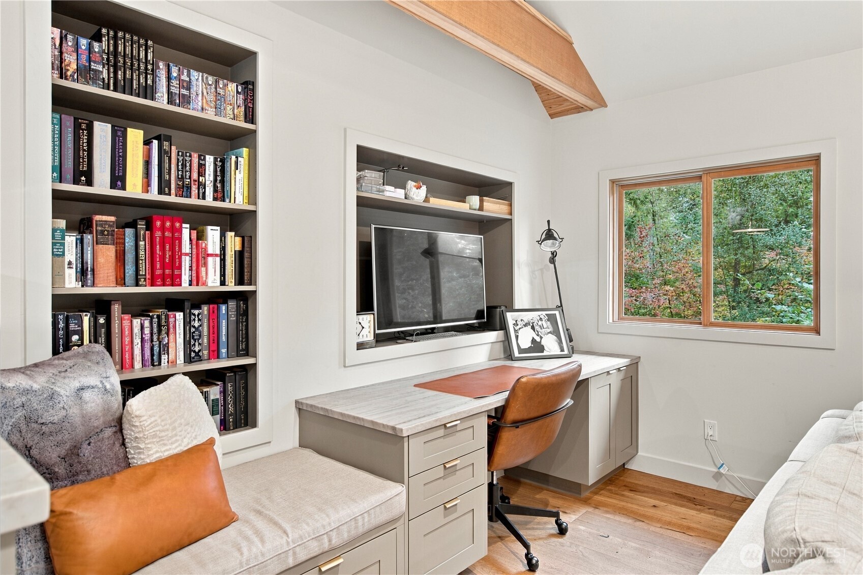 Home office with built-in bookcases, a desk, and a window overlooking trees.