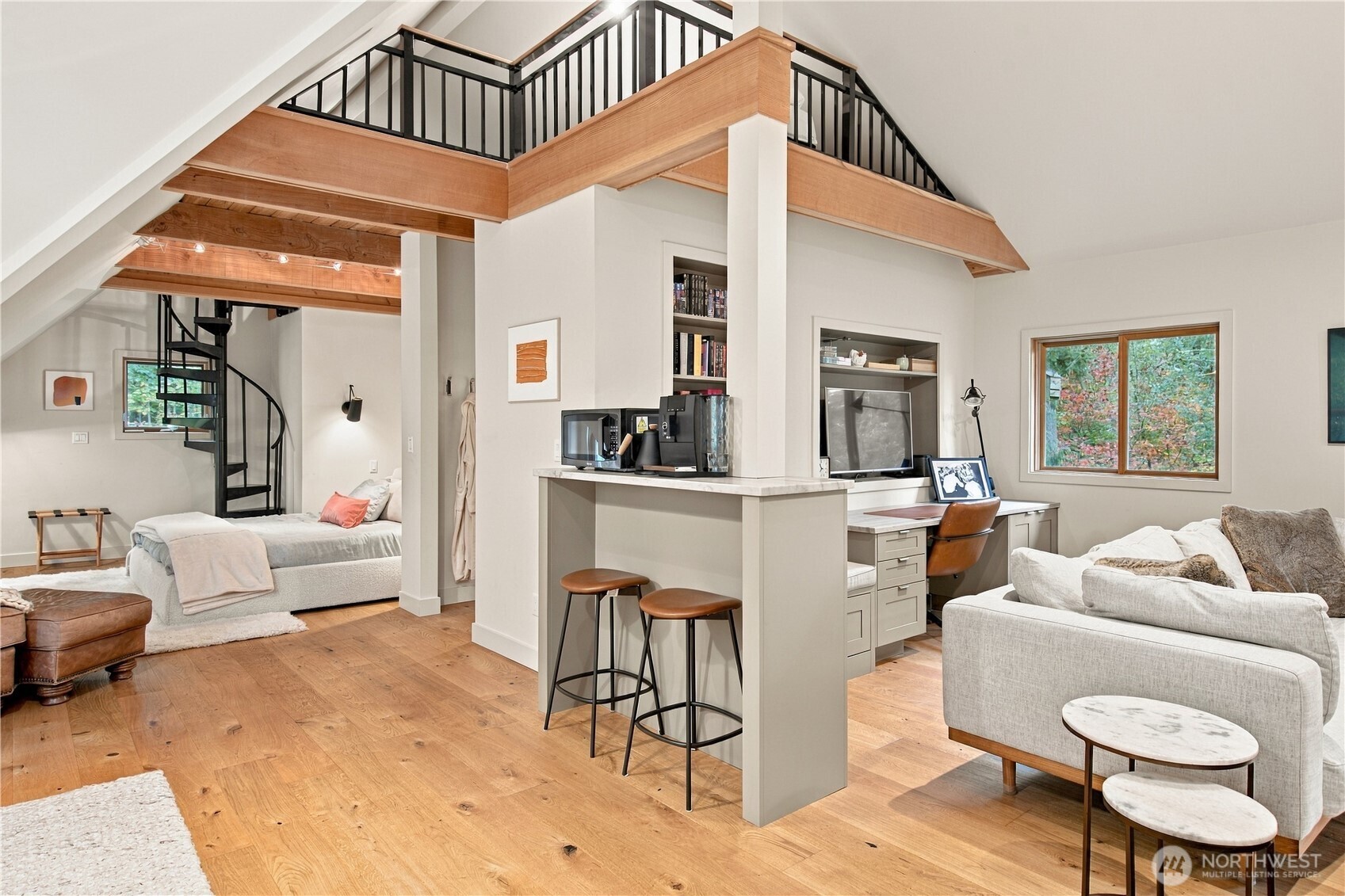 Open-plan living area with a loft, black spiral staircase, and kitchen island with stools.