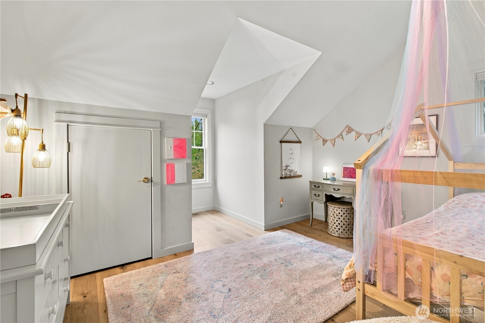 Bedroom with a wooden canopy bed draped in sheer pastel fabric and a pale patterned rug.