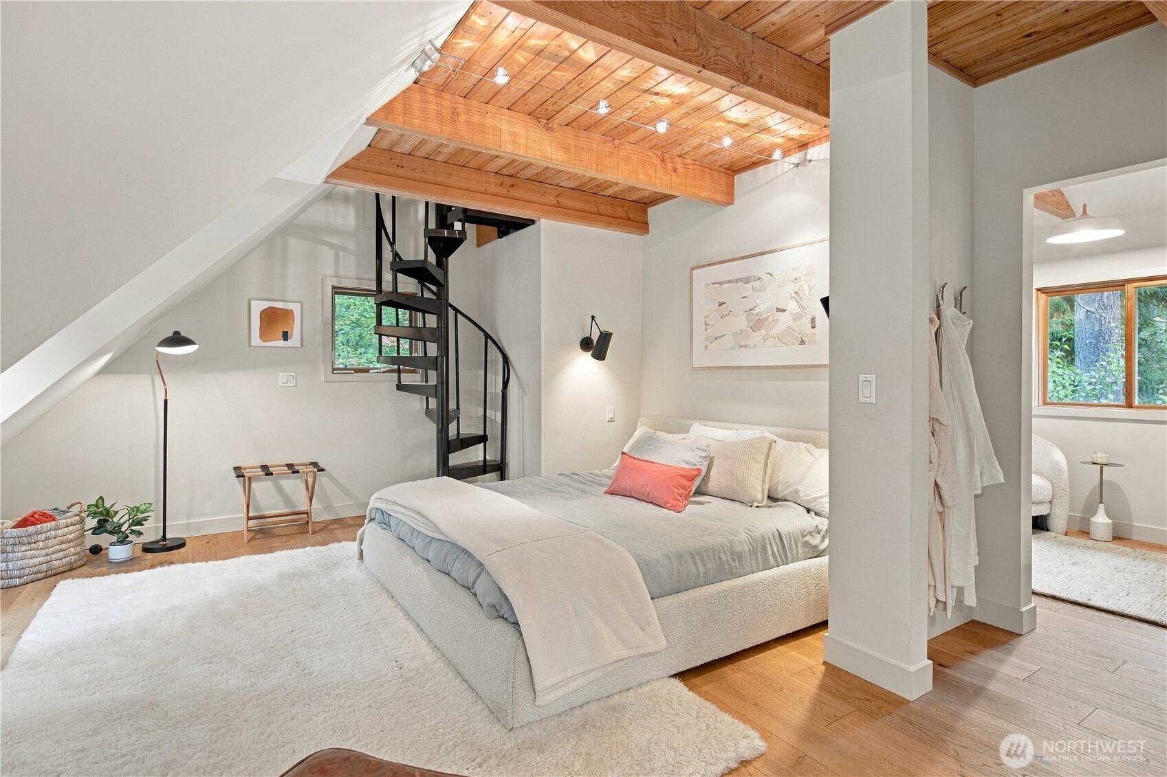 Bedroom with exposed wood ceiling, black spiral staircase, and bed on a white rug.