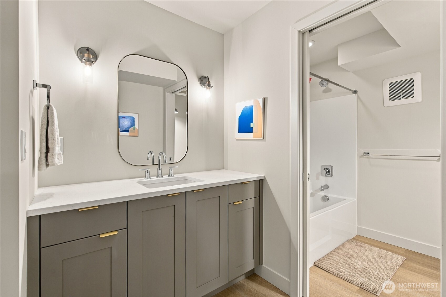 Bathroom with a gray vanity, arched mirror, and tub-shower behind a glass door.