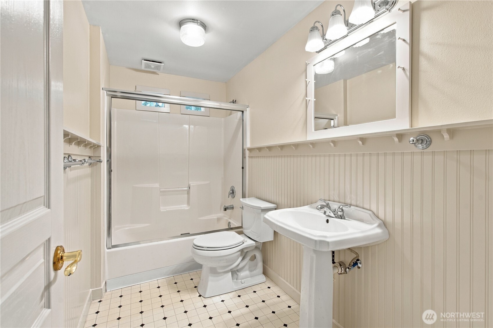 Bathroom with a white shower-tub, pedestal sink, beadboard walls, and black-accented tile floor.