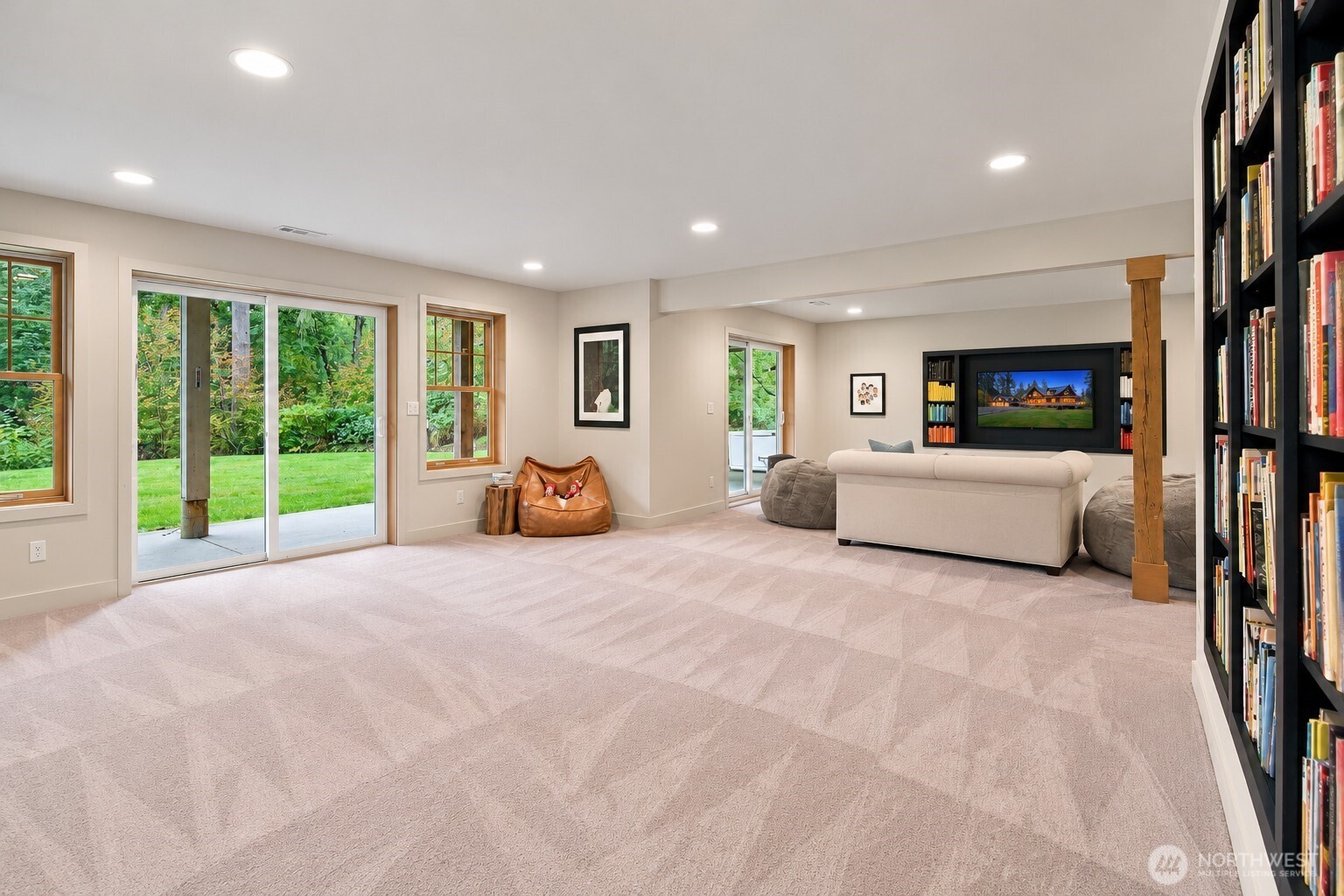 Furnished living room with built-in bookcase, media wall, and sliding glass doors overlooking a lawn.