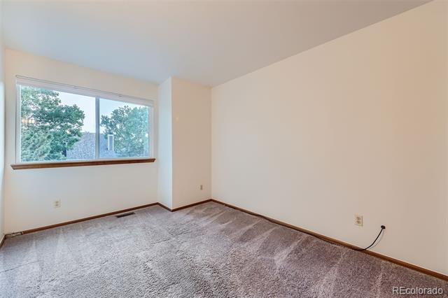 Empty carpeted bedroom with a wide window overlooking leafy trees.