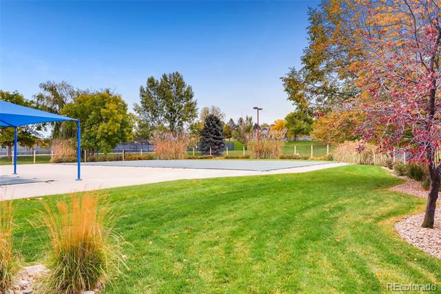 Landscaped outdoor recreation area with a blue shade canopy beside a broad lawn and autumn trees.