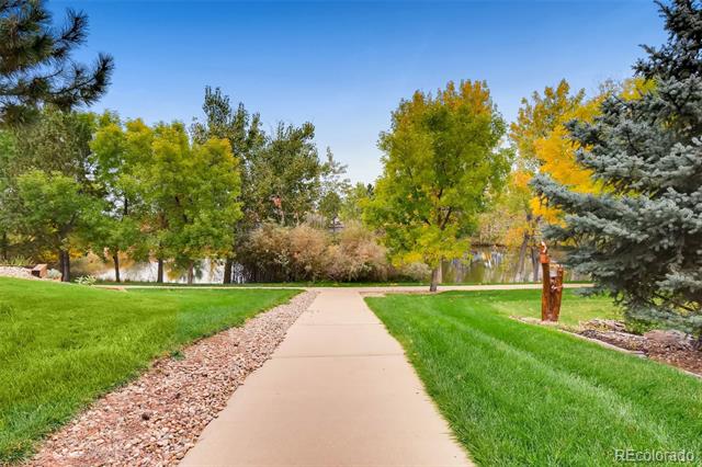 Paved walking path through landscaped grounds beside a pond, with autumn-colored trees.