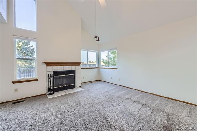 Empty living room with tall windows and a brick fireplace with a dark wood mantel.
