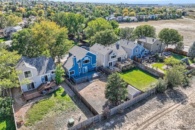 Aerial view of attached homes and fenced backyards bordered by autumn trees.