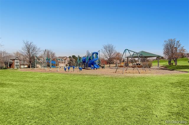 Neighborhood playground with blue slides and swings beside a broad green lawn.