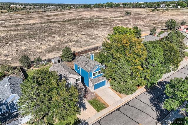 Aerial view of a blue two-story house beside a large open field, surrounded by mature trees.
