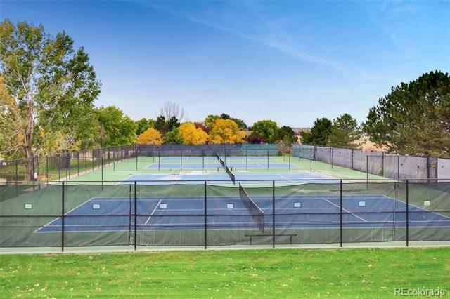 Fenced tennis courts with blue and green surfaces, grass, and autumn trees.