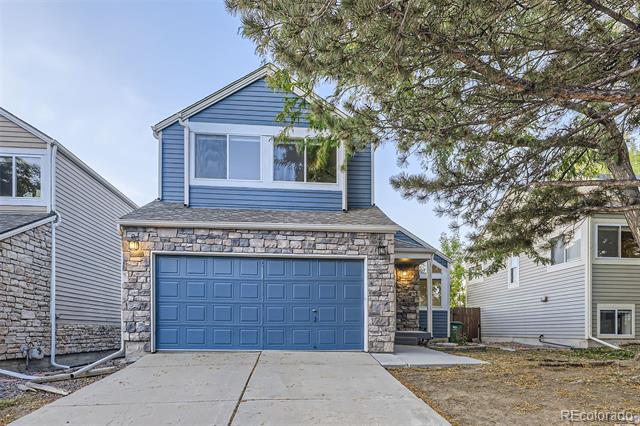 Two-story blue house with a stone-faced garage and a large pine tree overhanging the driveway.