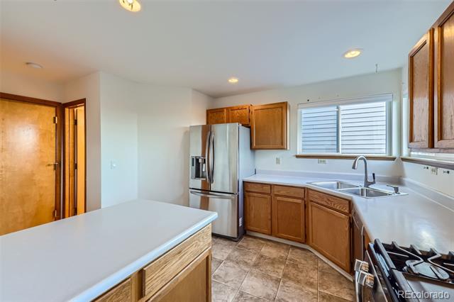 Kitchen with wood cabinets, white countertops, stainless steel refrigerator, and a sink beneath a shuttered window.