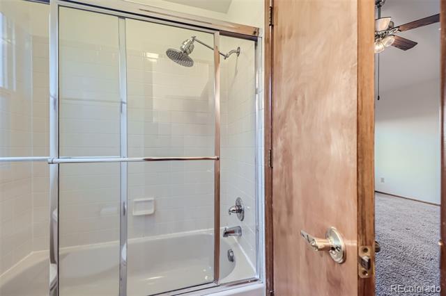 Bathroom with a white tiled shower enclosed by sliding glass doors and an open wooden door.