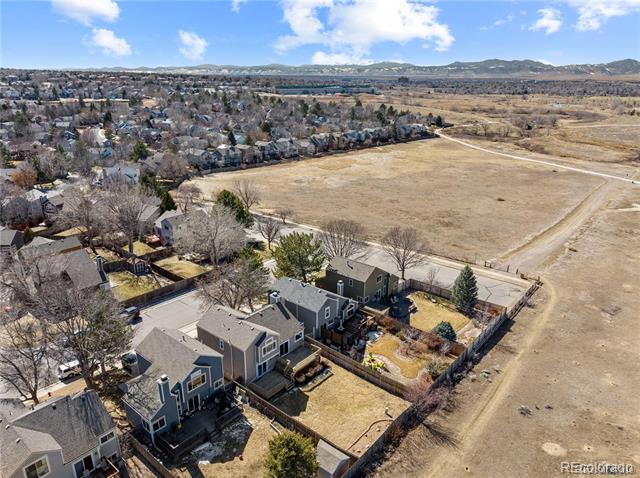 Aerial view of attached homes and fenced yards beside a large open field.