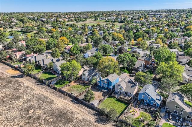 Aerial view of a leafy neighborhood, with blue houses beside a dry open lot.