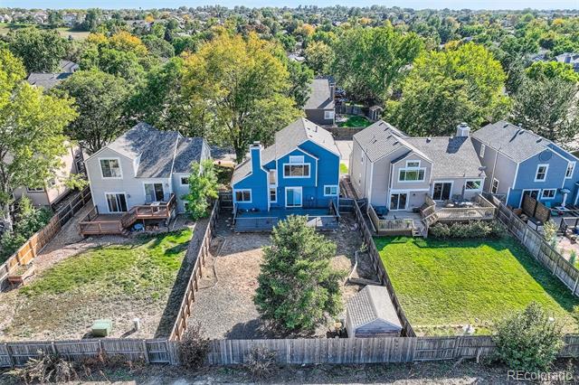 Blue two-story house viewed from behind, with a fenced gravel yard and neighboring homes.