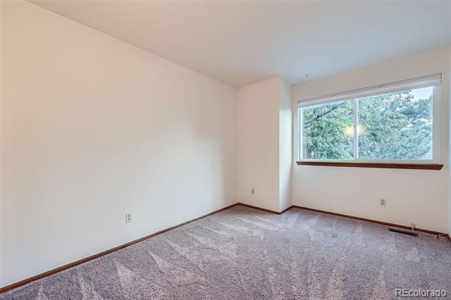 Empty bedroom with gray carpet, wood trim, and a wide window overlooking trees.