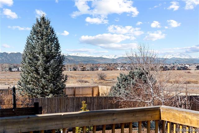 Mountain range beyond an open field, viewed over a fenced backyard and wooden deck railing.