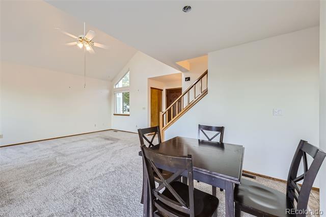 Open living and dining area with a vaulted ceiling, carpeted floor, and staircase.