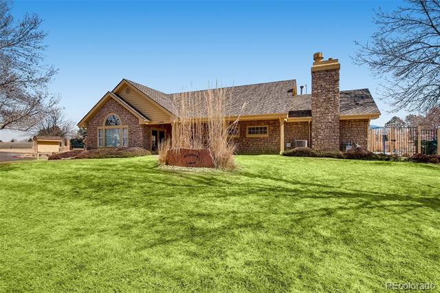 Single-story brick home with a stone chimney and broad green lawn.