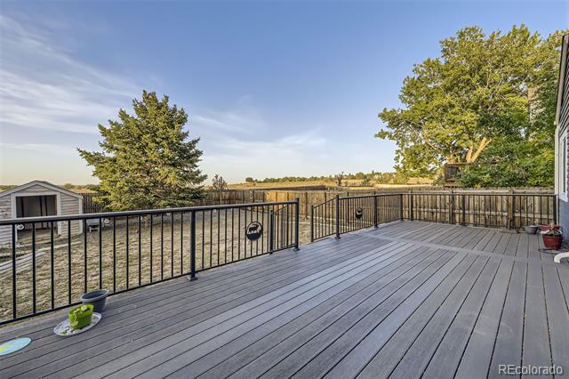 Gray deck with black railings overlooks a fenced yard and open land.