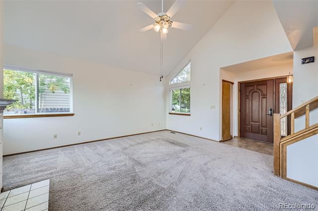 Vacant living room with vaulted ceiling, carpet, ceiling fan, and staircase by the front door.