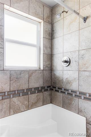 Tiled bathtub and shower with a white-framed window and decorative tile border.