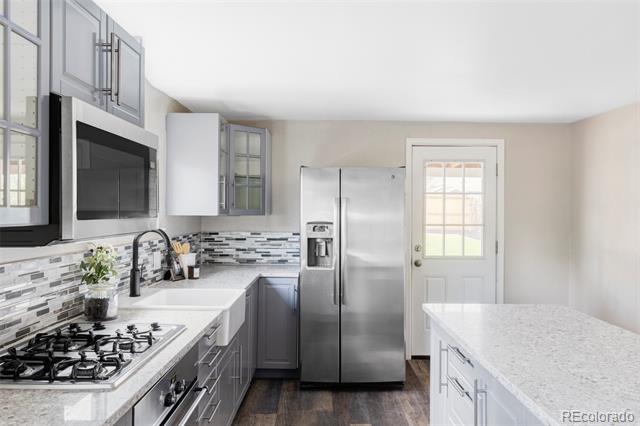 Bright kitchen with gray cabinets, stainless appliances, gas cooktop, and a long stone island.