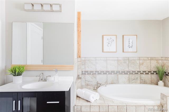 Bathroom with a tiled corner soaking tub beside a dark vanity and wide mirror.