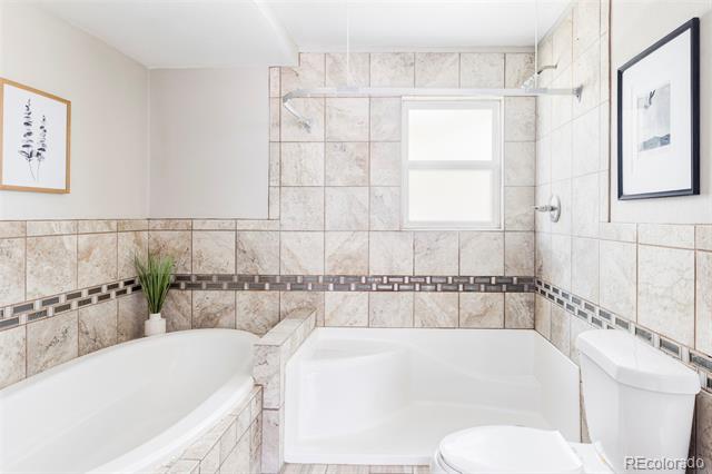 Tiled bathroom with a large corner tub, separate bathtub, and decorative dark tile border.
