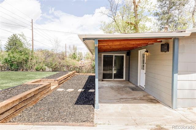 Covered concrete patio with sliding glass door and raised timber garden beds beside a gravel yard.