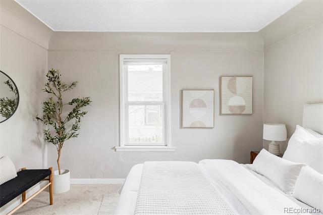 Bedroom with a white bed, central window, abstract prints, and potted tree.