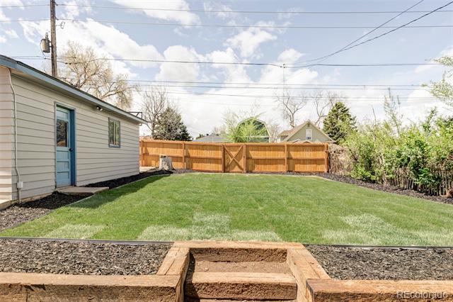 Backyard with a broad green lawn, wooden privacy fence and gate, and a blue side door.