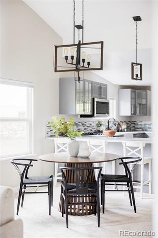 Bright kitchen and dining area with white cabinetry, stainless steel appliances, and a round table beneath pendant lights.