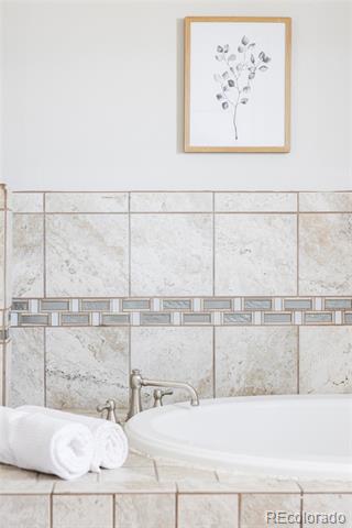 Bathroom with a white bathtub, rolled towels, and beige tile with a mosaic border.